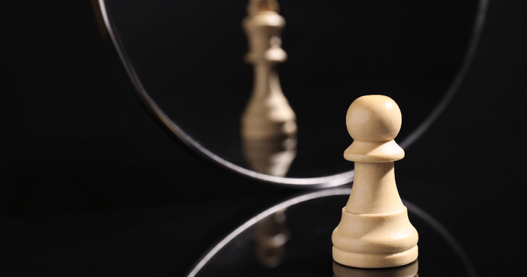 peão de xadrez em frente ao espelho refletindo imagem da peça rainha